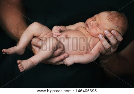 Father holding delicate his asleep newborn baby.