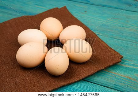 Chicken Eggs And Brown Linen Napkin On Blue Wooden Table