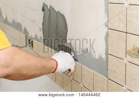 Worker instiling tiles on the wall in the kitchen. He put adhesive using a trowel.
