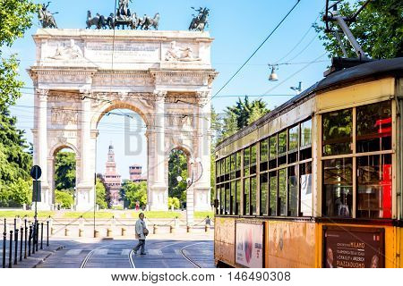 Milan, Italy - June 07, 2016: City view with elder woman cross the street, old tram and Simplon roman city gate in Milan city in Italy