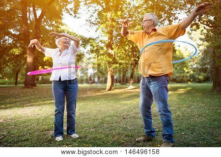 Happy Funny Senior Couple Playing Hulahop In Park