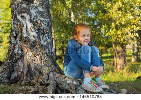 Little girl sitting on the roots of a birch.