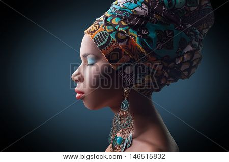 young beautiful fashion model with traditional african style with scarf, earrings and makeup on dark blue background.