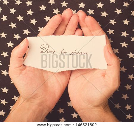 Woman with star patterned dress holding a note with dare to dream message on it