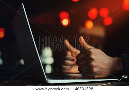 Black man's hands with thumbs up gesture. Gesture All is excellent. Person working with laptop. Beautiful lights as background. Toned style instagram filters.