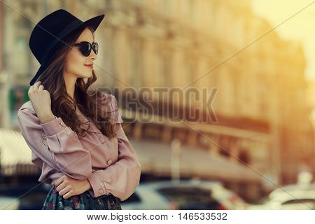 Outdoor portrait of young happy lady posing on street. Model wearing stylish clothes. Girl looking aside. Sunny day. Female fashion. City lifestyle. Toned style instagram filters. Copy space for text.
