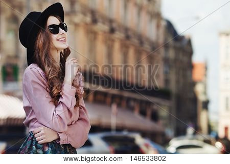 Outdoor portrait of a young beautiful fashionable happy lady posing on a street of the old city. Model wearing stylish clothes. Girl looking up. Female fashion. City lifestyle. Copy space for text.