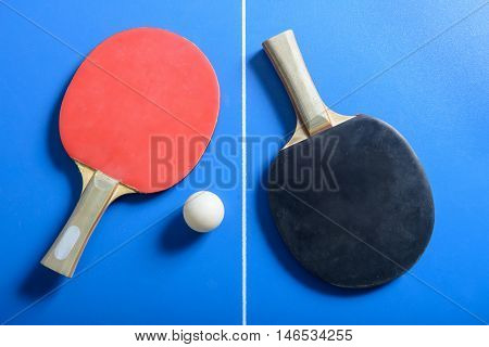 Pin-pong rubbers and a ball on blue playing board