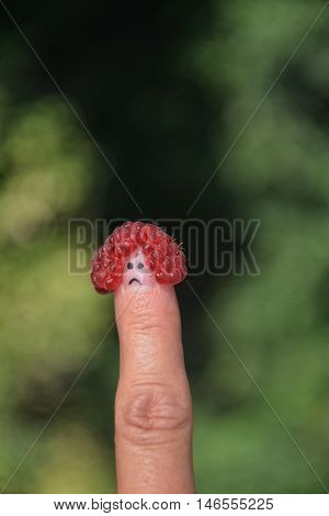 Red raspberry on the thumb with a sad face in front of green nature