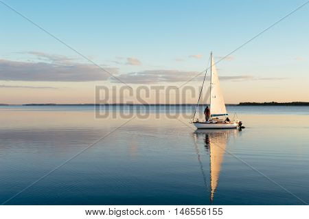 Sailing boat on a calm lake with reflection in the water. Serene scene landscape. Horizontal photograph.