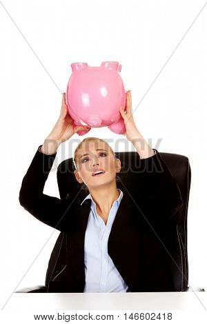 Worried business woman with a piggybank behind the desk