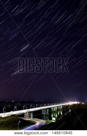 Scenic view with the bridge over the river and the stars in the form of tracks in the night sky shot on a long exposure