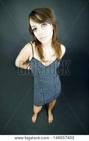 A young girl with dark hair and wearing a black and white polka dot dress looks up with longing eyes.