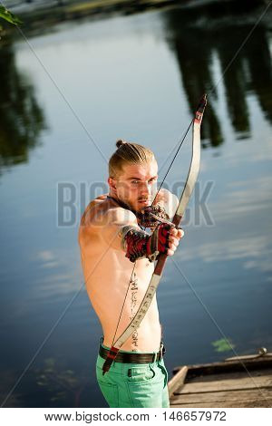 Male Archer on the banks of the river pulls the arrow