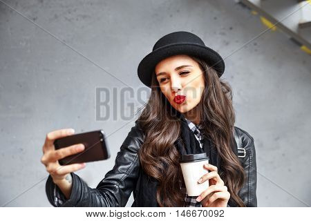 Pretty Hipster Girl With Red Lips And In Hat  Taking Selfie And Making Duck Face. Sending Kisses And