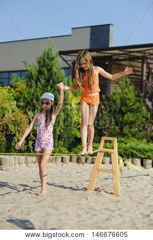 Two girls having fun on sling. Girl teenagers learn to walk on a tightrope with his girlfriend.