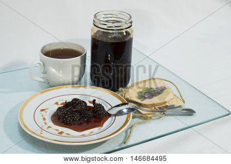 Jam made from pine cones on a plate and a cup of tea