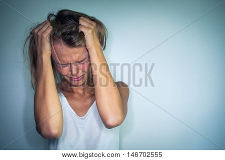 Young woman suffering from a severe depression, anxiety/sudden fear (very harsh lighting is used on this shot to underline/convey the gloomy mood of the scene; color toned image)