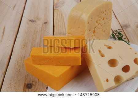 various types of fresh raw aged delicatessen cheese on white plate over light wooden table cheddar swiss