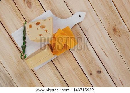 various types of fresh raw aged delicatessen cheese on white plate over light wooden table cheddar swiss