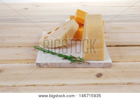 various types of fresh raw aged delicatessen cheese on white plate over light wooden table cheddar swiss