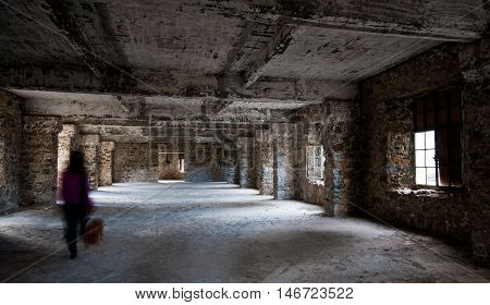Unrecognized person walks like a ghost on an empty creepy abandoned hotel room with dramatic sun rays entering through the windows.
