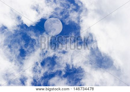 Moon clouds is a daytime scenic of wispy white cumulus clouds set against a deep blue sky as a full moon rises in the sky.
