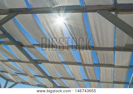 White beach canopy made of white pieces of cloth. Sunlight breaks through the protection.