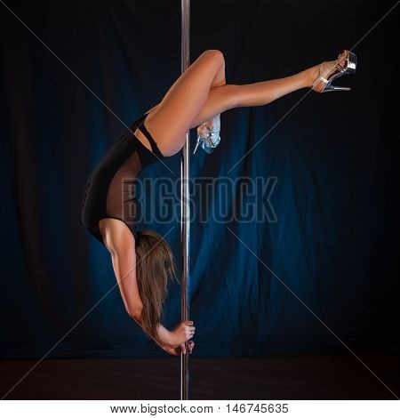 sexy young slender brunette dancing on the pole. Female caucasian appearance with an excellent bum shows tricks on the pole