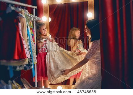 Cute little fashionista. Young mother and her daughter child girl try on outfits and look at mirror.