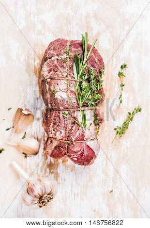 Raw uncooked roastbeef meat cut with rosemary, thyme and garlic on old white painted wooden background, top view, selective focus