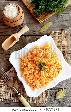 Vegetable risotto on a plate, fork, green dill, cutting board on old wooden background. Rice cooked with tomatoes, carrots, garlic and spices. Easy vegetarian risotto recipe