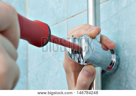 Residential plumbing repair close-up of hands handyman with red phillips screwdriver install adjustable shower slide rail bar bracket.