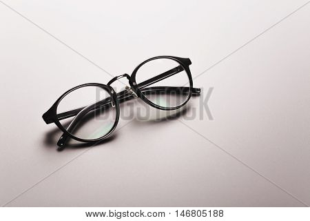 Black satine plastic circle eye glasses for womenor hipster, lying on grey background with accurate shadow.