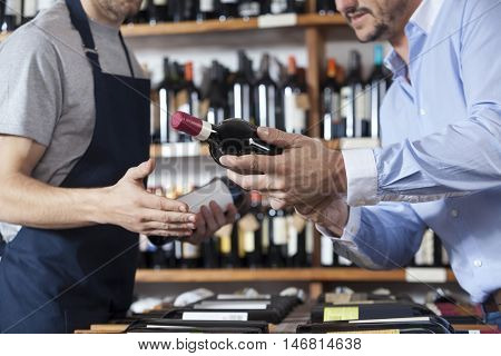 Midsection Of Customer Showing Wine Bottle To Salesman
