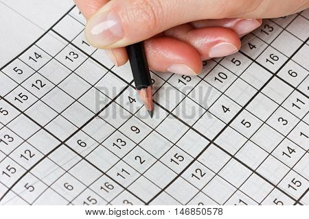 Woman hand holding a pencil and solves crossword sudoku. Popular puzzle game with numbers.