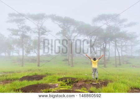 Happy young man is spreading hand and enjoying morning mist in forest before sunrise. Bolaven plateau Southern of LAOS