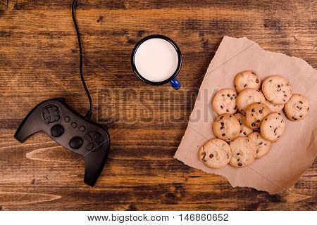 Gamepad and homemade chocolate chip cookies on rustic wooden table top view concept of childhood memories and nostalgia.