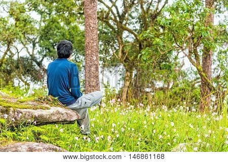 Young man relaxing and enjoying with flower field while sitting on the rock.