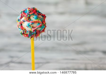 Bright cake lollipop. Glazed candy on stick. Taste of cheerful life. Congratulate a kid with birthday.