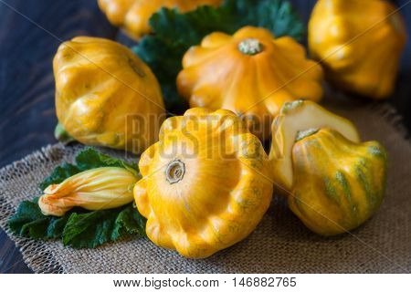 three yellow pattypan squash with leaf and flower on a dark wooden table.