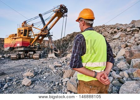 Worker looks on excavator works at opencast
