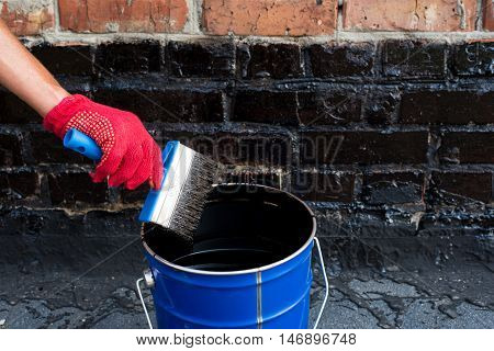 Roofer covered brick wall bitumen primer for improving adhesion during surfacing contiguity with rolled waterproofing during the installation of flat roof.