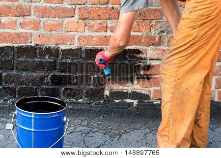 Roofer covered brick wall bitumen primer for improving adhesion during surfacing contiguity with rolled waterproofing during the installation of flat roof.
