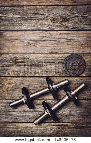 Old iron dumbbells or exercise weights with extra plates on an old wooden deck, floor or table. Image taken from above, top view. A lot of copy space around product