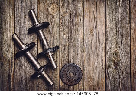 Old iron dumbbells or exercise weights with extra plates on an old wooden deck, floor or table. Image taken from above, top view. A lot of copy space around product