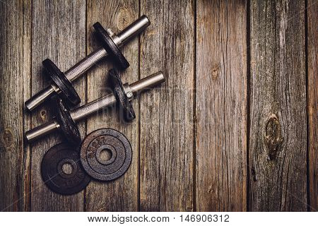 Old iron dumbbells or exercise weights with extra plates on an old wooden deck, floor or table. Image taken from above, top view. A lot of copy space around product
