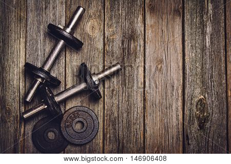 Old iron dumbbells or exercise weights with extra plates on an old wooden deck, floor or table. Image taken from above, top view. A lot of copy space around product