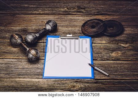 Old iron dumbbells or exercise weights with extra plates on an old wooden deck, floor or table. Image taken from above, low angle . A lot of copy space around product