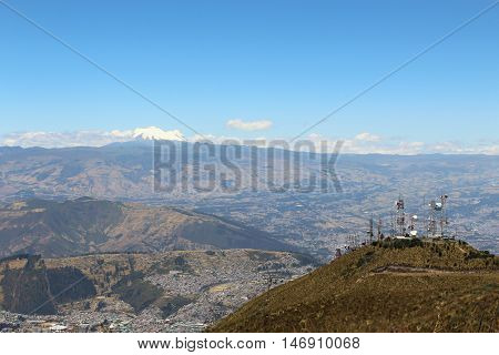 This photo shows a view of the Antisana Volcano in the background, part of the Quito city and the cableway station on Quito, Ecuador.